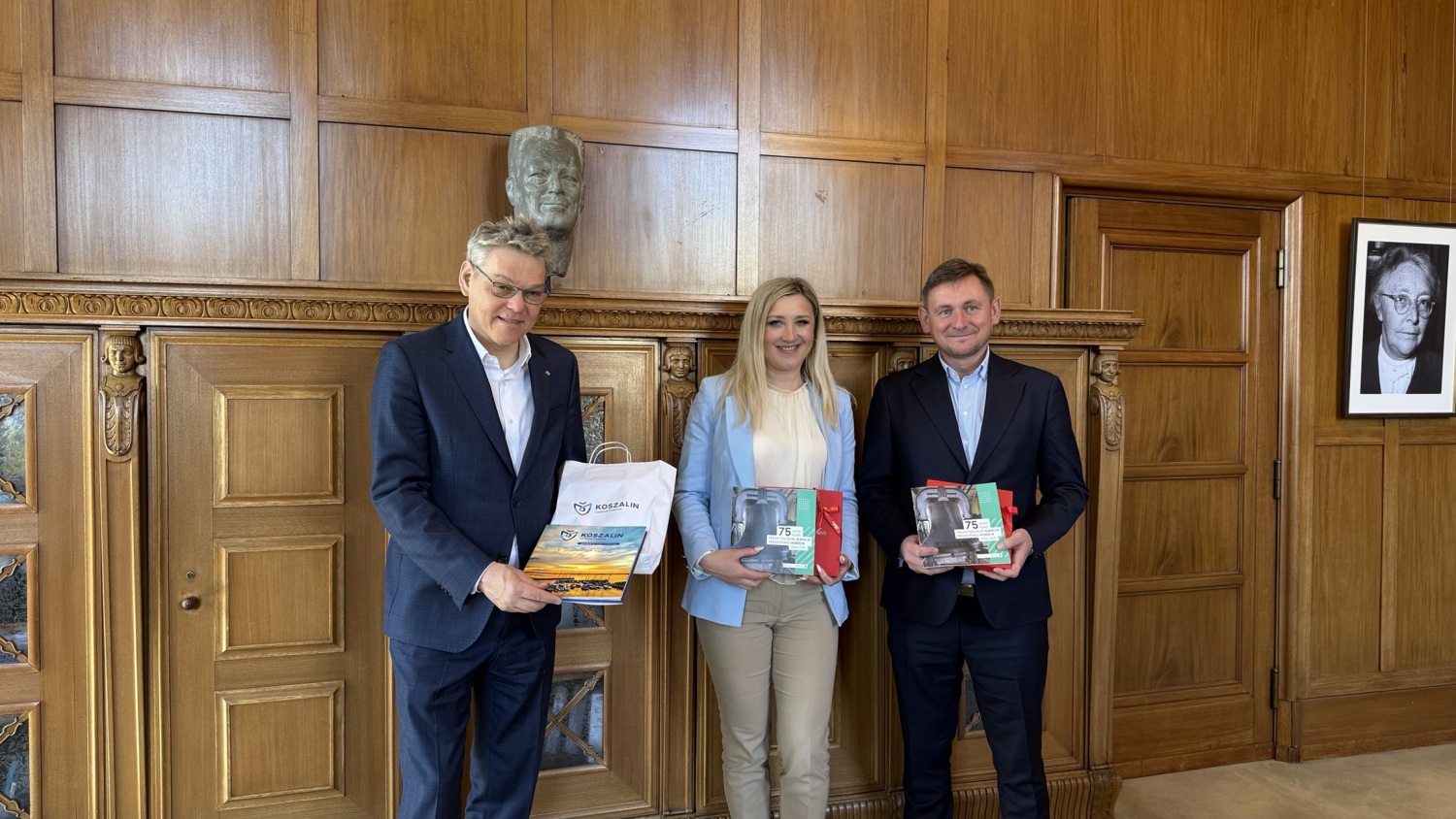 Drei Personen stehen nebeneinander in einem Raum und halten Broschüren in den Händen.