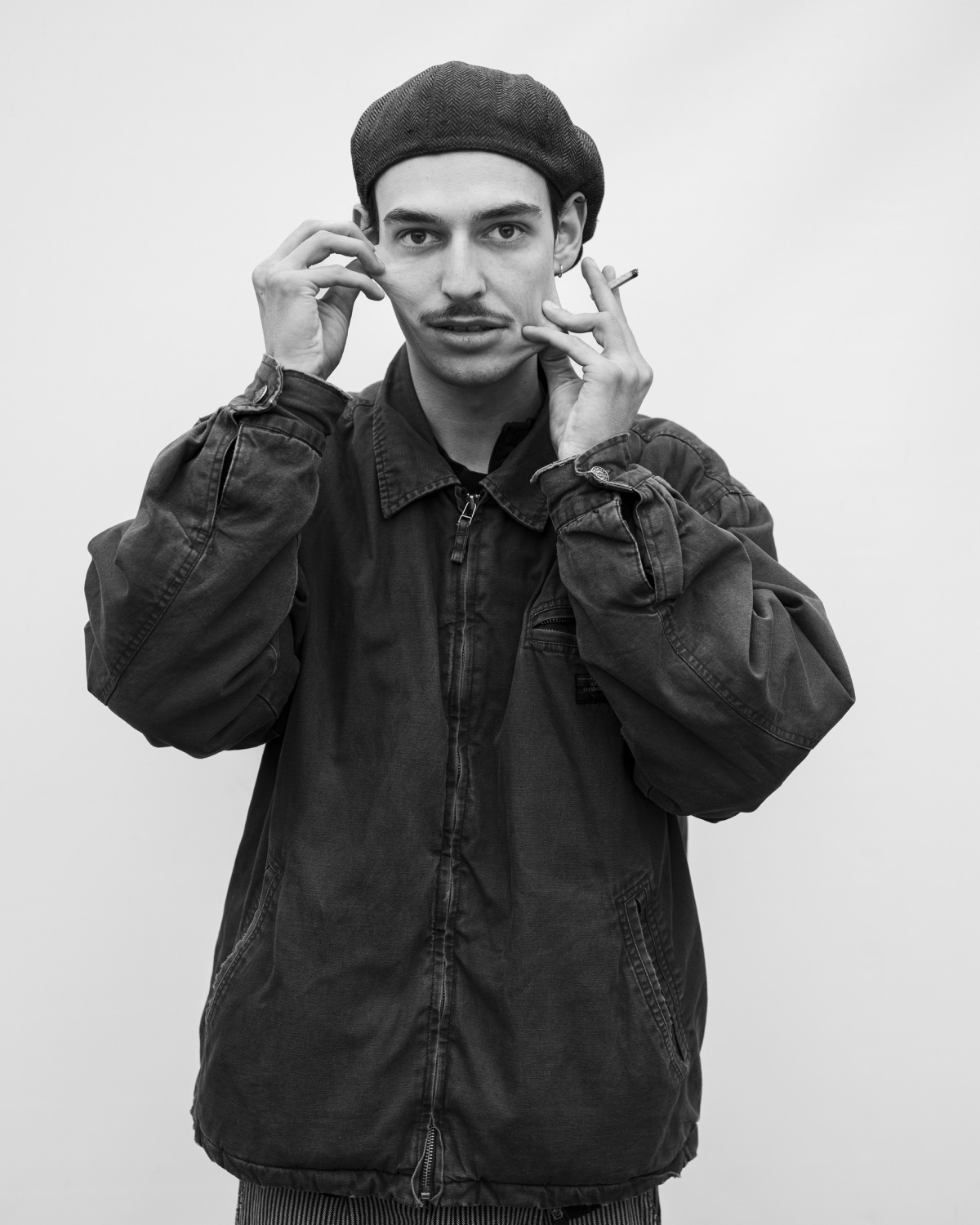 Schwarzweißfotografie eines Mannes, der an seinem eigenen Gesicht zieht; in einer Hand ist eine angefangene Zigarette