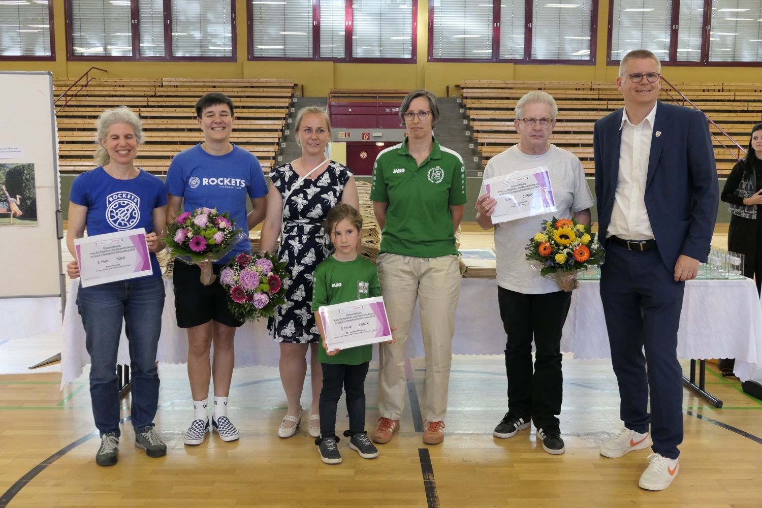 Personen mit Urkunden und Blumensträußen in einer Sporthalle