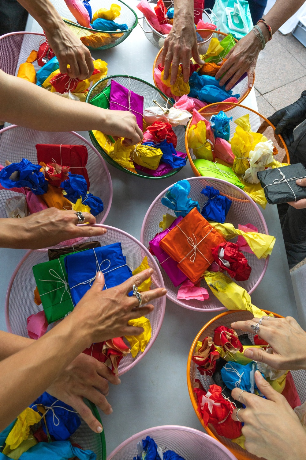 Viele Hände greifen in bunte Schalen, welche mit kleinen ebenfalls bunt verpackten Süßigkeiten und Naschereien gefüllt sind.
