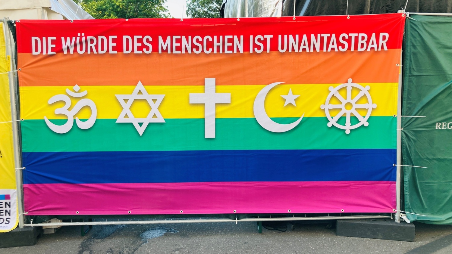 Großes Banner in Regenbogenfarben mit den verschiedenen Religionssymbolen und dem Spruch "Die Würde des Menschen ist unantastbar"