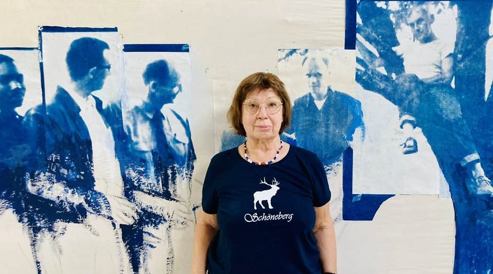 Eine Frau steht mit dem Rücken zu einer Wand, auf der Kunstwerke hängen.