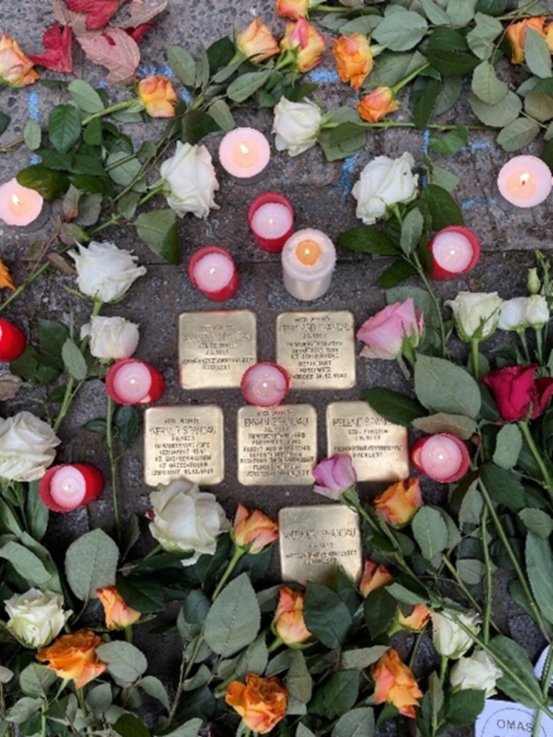 Kerzen und Blumen liegen auf einem Gehweg mit Stolpersteinen