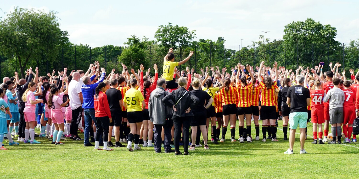 Viele Jugendliche stehen auf einem Fußballfeld und jubeln.