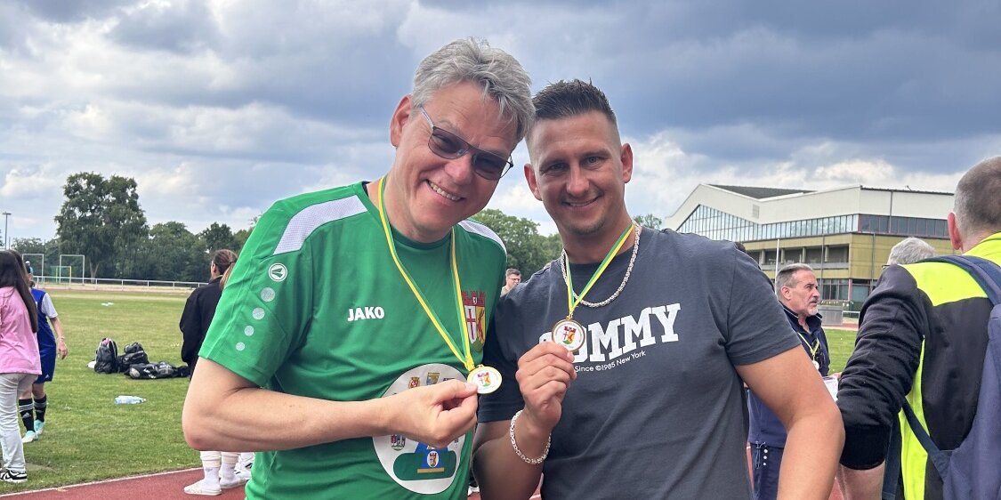 Zwei Personen präsentieren die gewonnene Medaille.