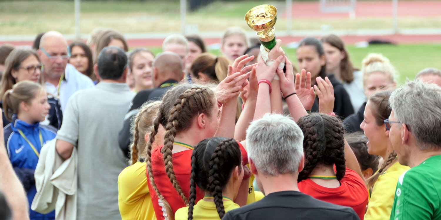 Ein Mädchenteam jubelt und streckt den gewonnenen Pokal in die Höhe.
