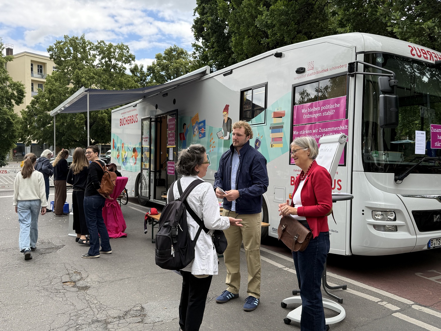 mehrere Menschen stehen vor einem bunten Bus und sprechen miteinander