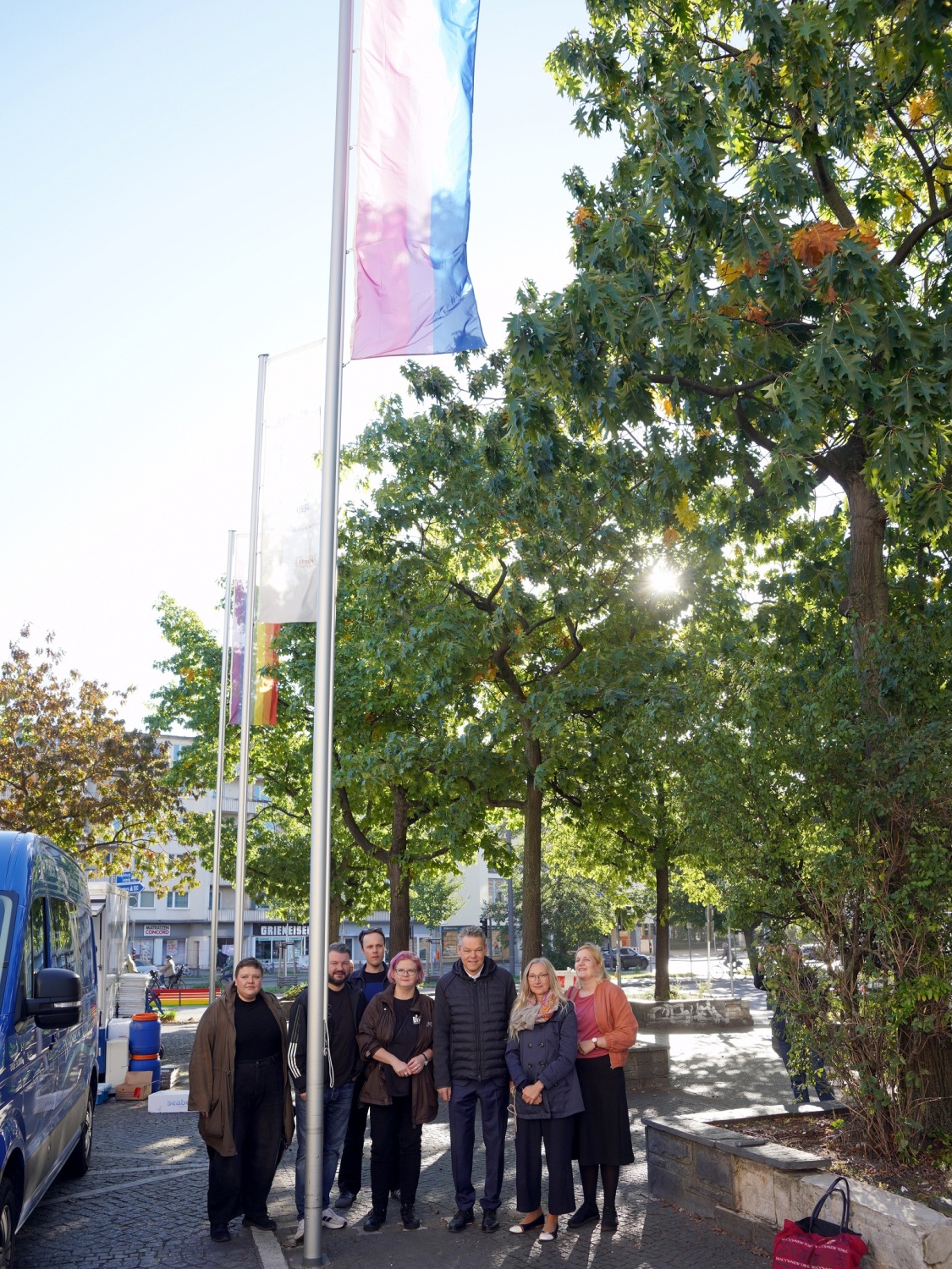 Mehrere Personen stehen am Fuße eines Fahnenmastes, an dem eine Flagge hängt.