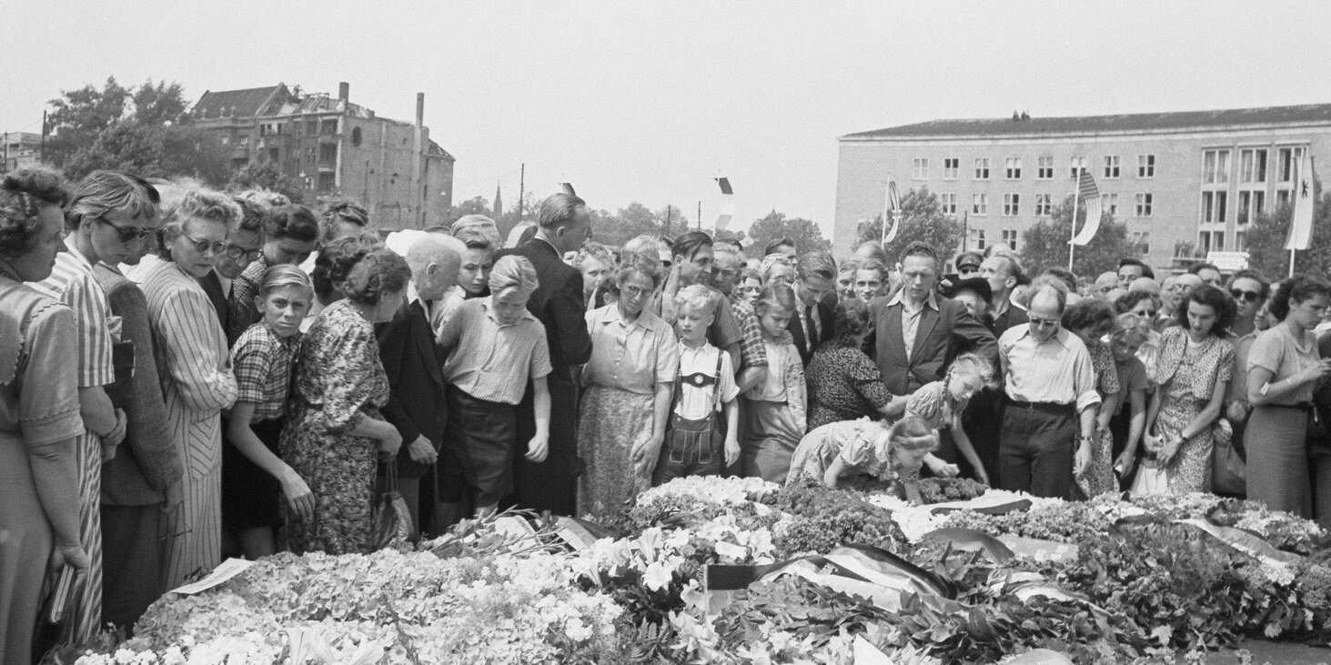 viele Menschen stehen vor großen Blumenkränzen