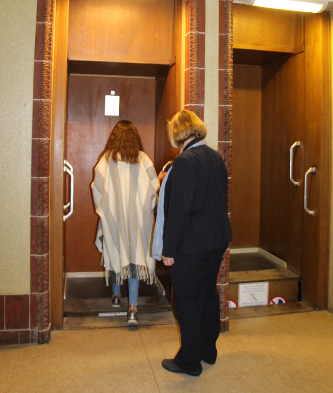 Tuana Lingnau steigt in den Paternoster während Bezirksbürgermeisterin Angelika Schöttler hinter ihr steht