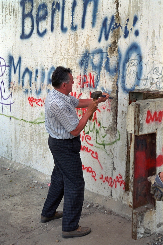 ein Mann schlägt mit Hammer und Meißel Stücken aus einer bemalten Betonwand