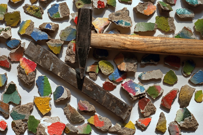ein Hammer und ein Meißel umgeben von kleinen bunten Betonteilen