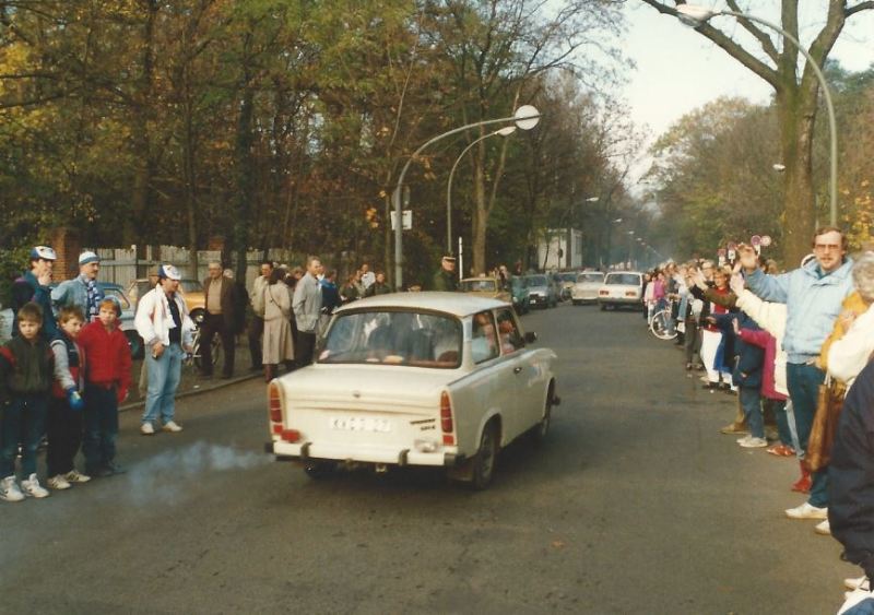 ein Auto fährt an winkenden menschen vorbei.
