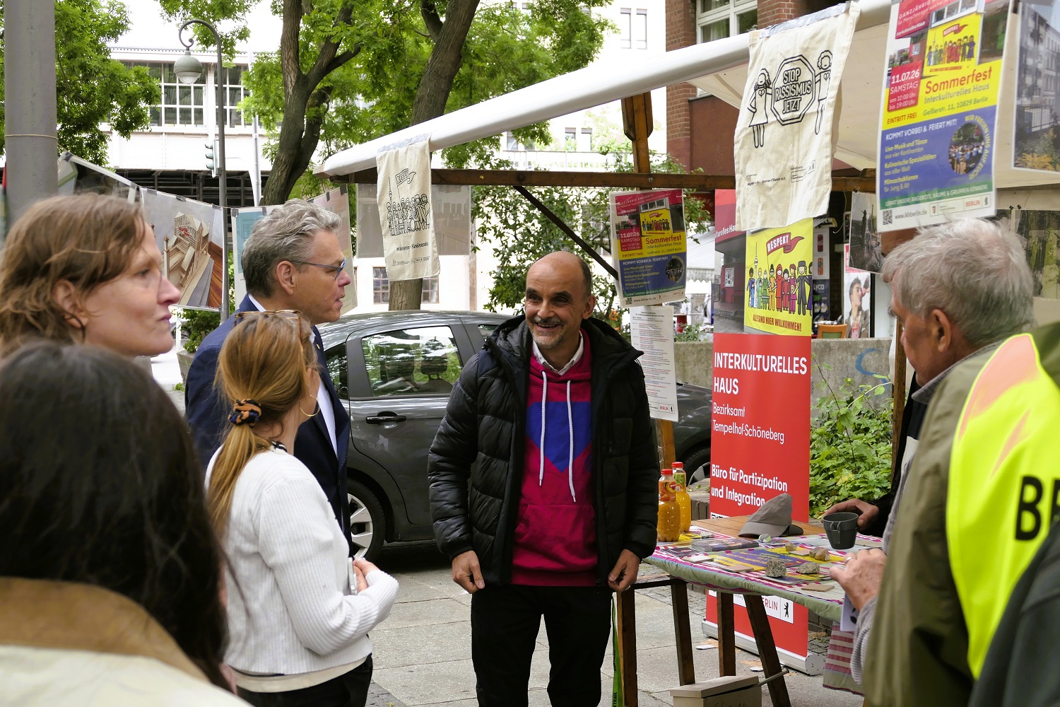 Mehrere Menschen stehen an einem Marktstand und unterhalten sich