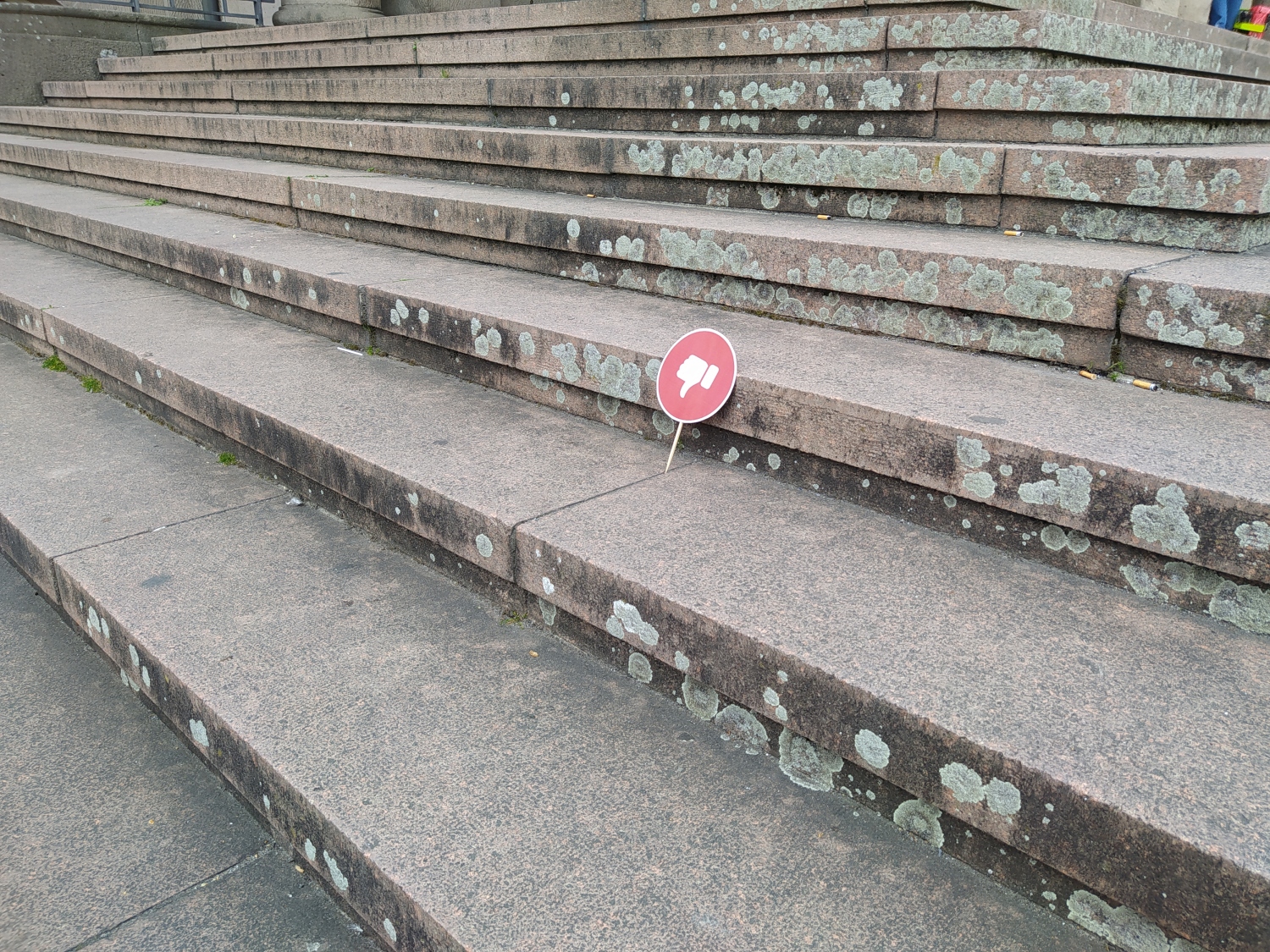 Auf dem Bild ist eine Steintreppe zu sehen. In den Fugen ist ein rundes rotes Schild eingehängt, auf dem ein Daumen, der nach unten zeigt, zu sehen ist.