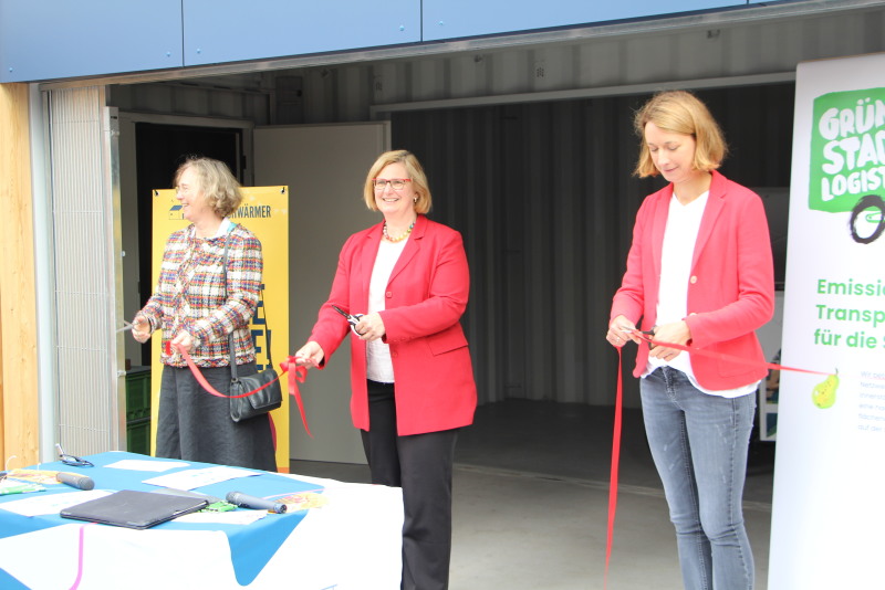 Drei Frauen schneiden das rote Band vor dem MicroHub durch. 