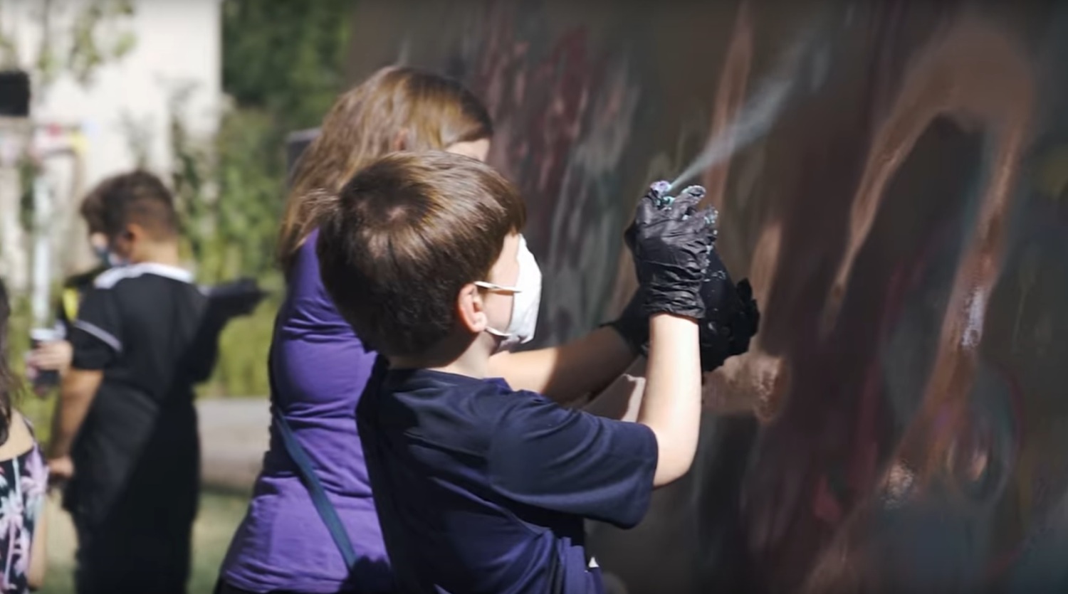 Ein Junge sprüht ein Graffiti an die Wand.