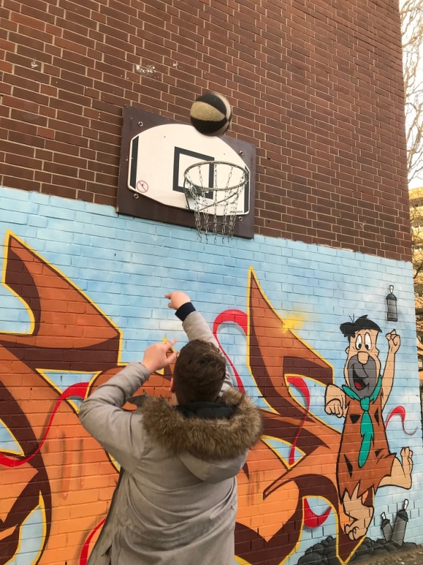 Jugendliche spielen Basketball an einem Basketball-Korb, der an einer Graffiti-Wand befestigt ist.