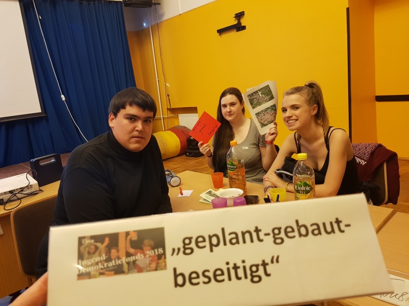 Drei Jugendliche halten Schilder und Urkunden in die Kamera.