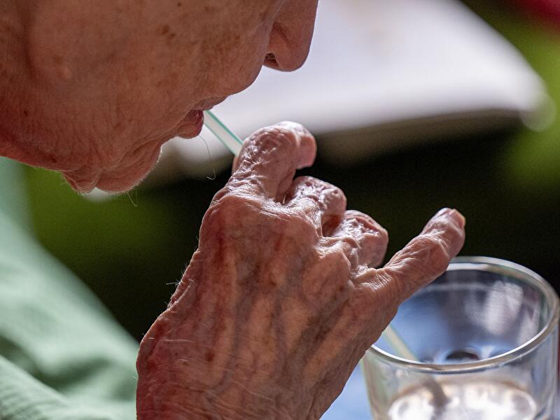 Nahaufnahme einer älteren Person, die mit einem Strohhalm aus einem Glas trinkt.