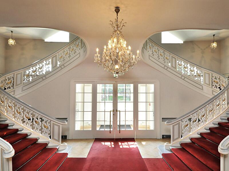 Prunkvolle doppelläufige Treppe im Schloss Schönhausen mit rotem Teppich, Kronleuchter und Glastüren.