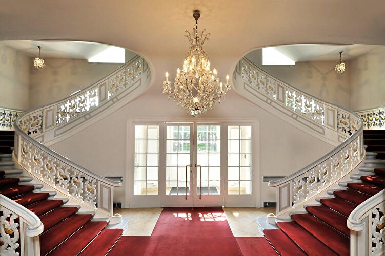 Prunkvolle doppelläufige Treppe im Schloss Schönhausen mit rotem Teppich, Kronleuchter und Glastüren.