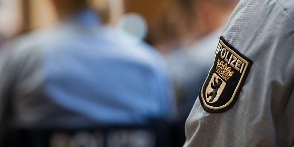 !Nahaufnahme einer Berliner Polizeiuniform mit Ärmelabzeichen, weitere Einsatzkräfte unscharf im Hintergrund.
