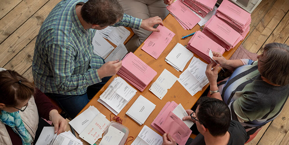 People are sorting and counting absentee ballot materials at a table with pink ballots