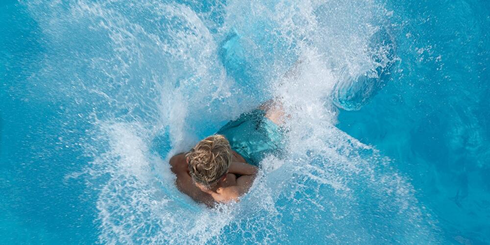 A boy jumps into the water at the swimming pool.