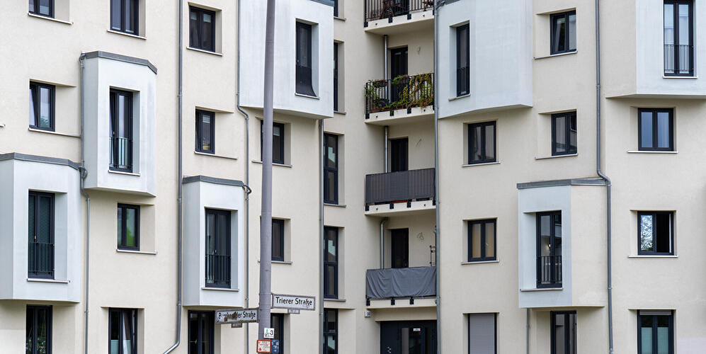 Mehrgeschossiges Wohngebäude mit Balkonen, Fenstern und heller Fassade an einer Straßenecke