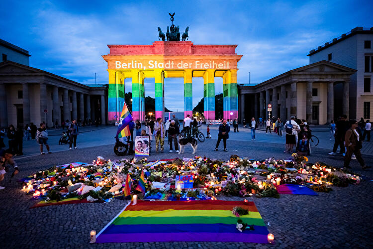 Brandenburger Tor in Regenbogenfarben, davor Kerzen, Blumen und Pride-Flaggen