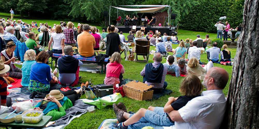 Visitors are sitting on a lawn in front of a stage, listening to music.