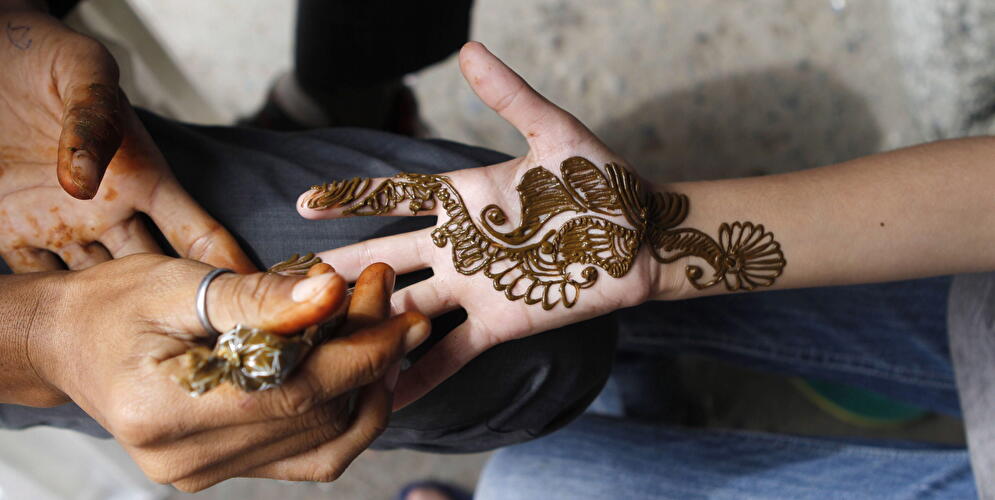 Eine Person bekommt ein florales Tattoo auf ihre Hand gemalt.