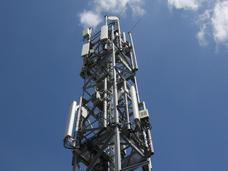 Mobilfunkmast mit Antennen vor blauem Himmel und wenigen weißen Wolken.