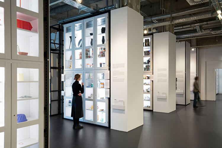 Person betrachtet Exponate in beleuchteten Vitrinen eines offenen Museumsdepots.
