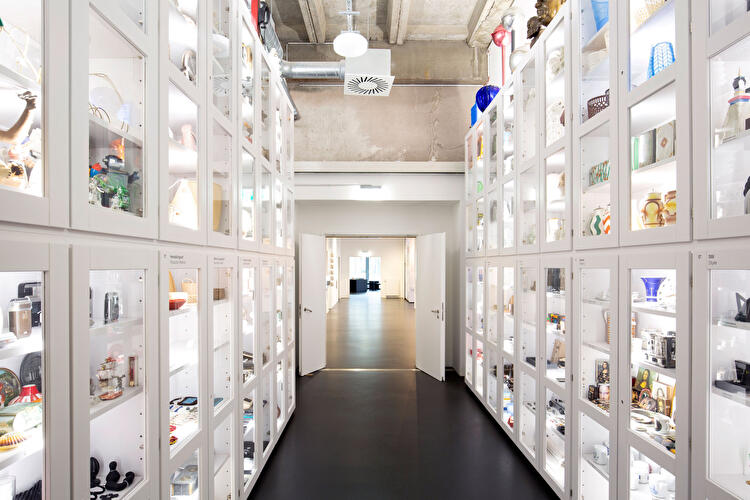 Gang mit beleuchteten Vitrinen voller Design- und Alltagsobjekte im Museumsdepot.