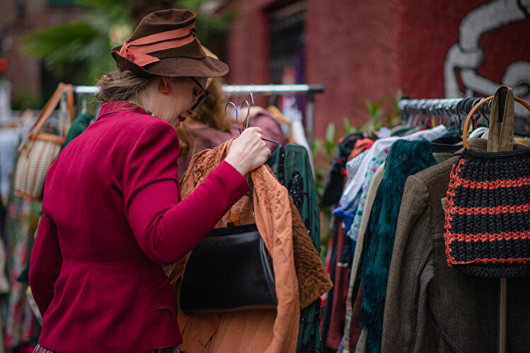 Eine Person betrachtet Kleidungsstücke an einem Kleiderständer auf einem Secondhand-Markt.