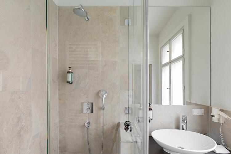 Badezimmer mit gefliester Dusche, freistehendem Waschbecken und großem Wandspiegel, im Hintergrund ein Sprossenfenster.