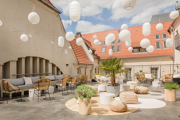Dachterrasse des Hotel Oderberger mit Rattanmöbeln, Pflanzen und zahlreichen Papierlaternen, umgeben von Altbaudächern unter blauem Himmel.