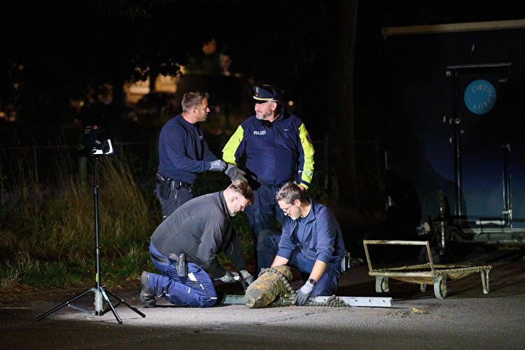 Mitglieder des Kampfmittelräumdienstes und ein Polizist knien nachts auf einer Straße um die geborgene Fliegerbombe, die auf einer Schiene liegt.