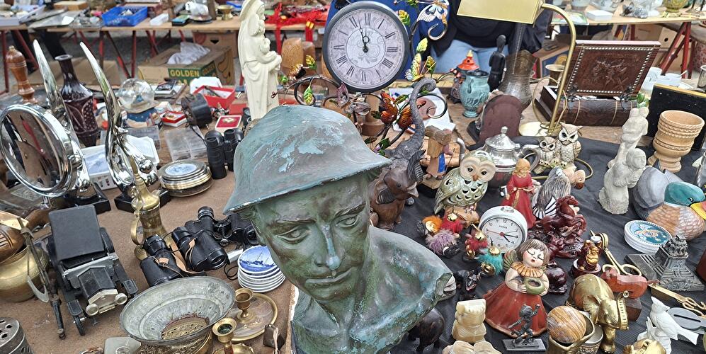 Rund um die bronzene Büste eines Soldaten liegen diverse Flohmarktartikel, die zum Kauf angeboten werden, auf dem Tisch.