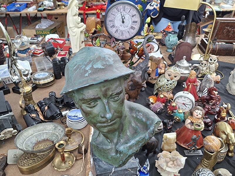 Rund um die bronzene Büste eines Soldaten liegen diverse Flohmarktartikel, die zum Kauf angeboten werden, auf dem Tisch.