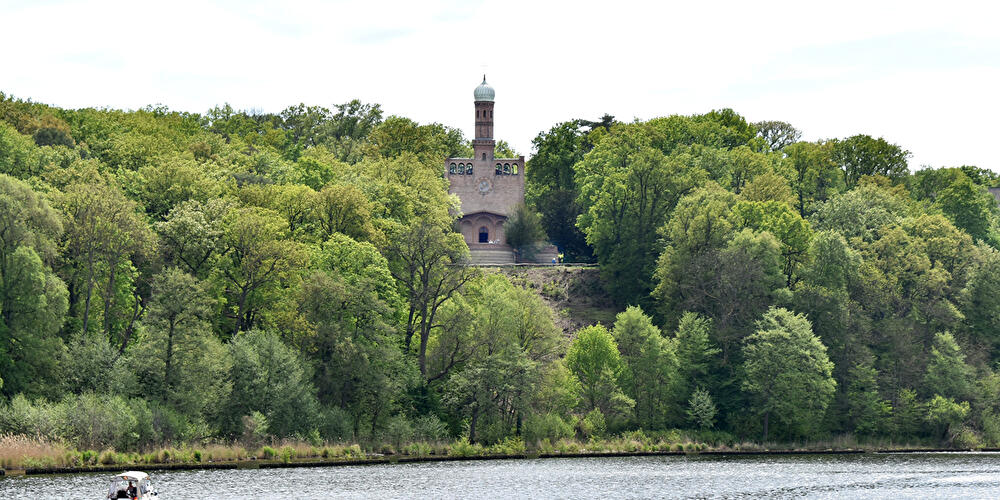 Die Kirche St. Peter und Paul umgeben von Bäumen von einem See aus betrachtet.