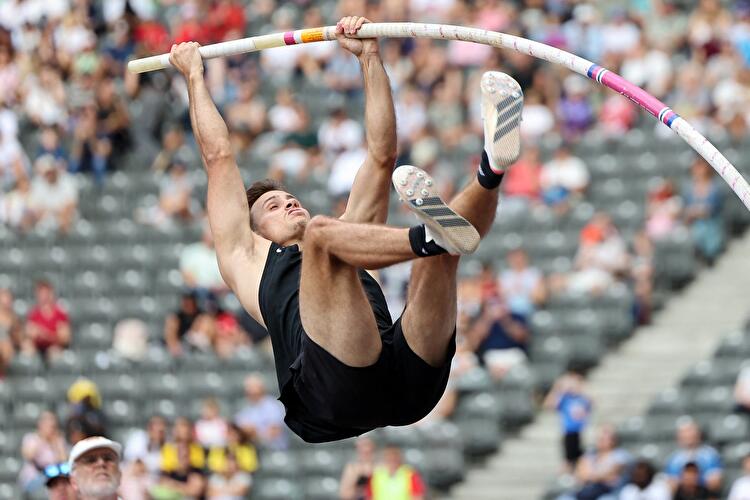 Ein Stabhochspringer schwingt sich beim ISTAF Berlin über die Latte, die Zuschauertribüne im Hintergrund.
