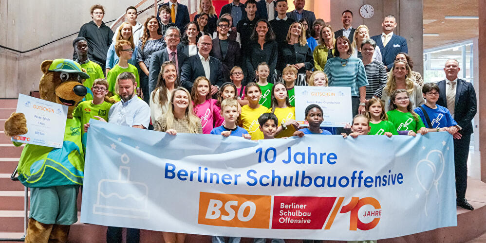 Kinder Berliner Schulen sowie Regierender Bürgermeister Kai Wegner, Bildungssenatorin Katharina Günther-Wünsch und Bausenator Christian Gaebler feiern mit einem Transparent "10 Jahre Berliner Schulbauoffensive" im Heinrich-Hertz-Gymnasium.