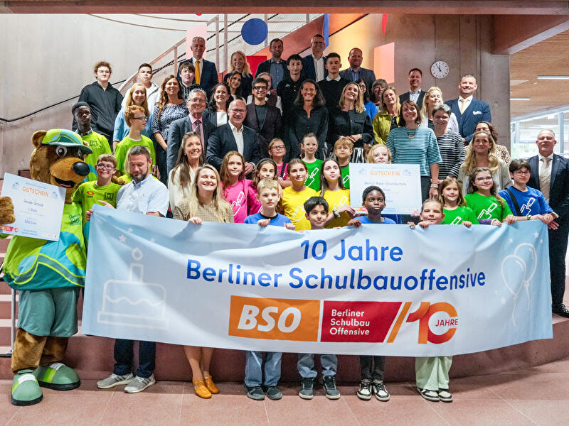 Kinder Berliner Schulen sowie Regierender Bürgermeister Kai Wegner, Bildungssenatorin Katharina Günther-Wünsch und Bausenator Christian Gaebler feiern mit einem Transparent "10 Jahre Berliner Schulbauoffensive" im Heinrich-Hertz-Gymnasium.