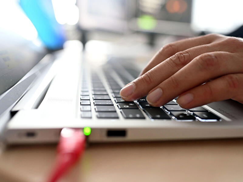 Hand tippt auf Laptop-Tastatur, Netzwerkanschluss mit Kabel im Vordergrund.