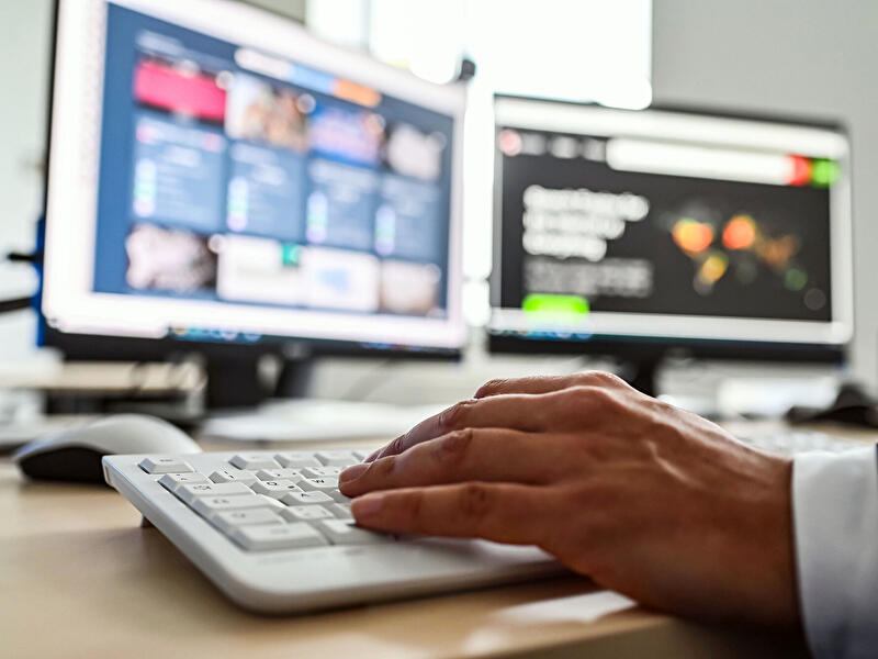 Hand an Computertastatur vor Monitoren mit IT- und Sicherheitsanzeigen.