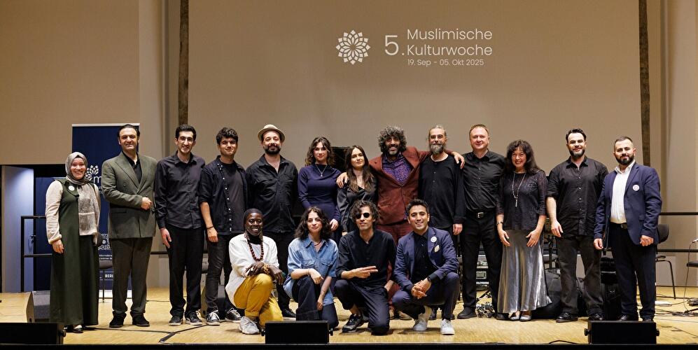 Gruppenfoto der Mitwirkenden der 5. Muslimischen Kulturwoche 2025 auf einer Bühne vor Veranstaltungslogo.
