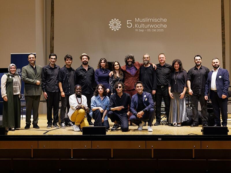 Gruppenfoto der Mitwirkenden der 5. Muslimischen Kulturwoche 2025 auf einer Bühne vor Veranstaltungslogo.